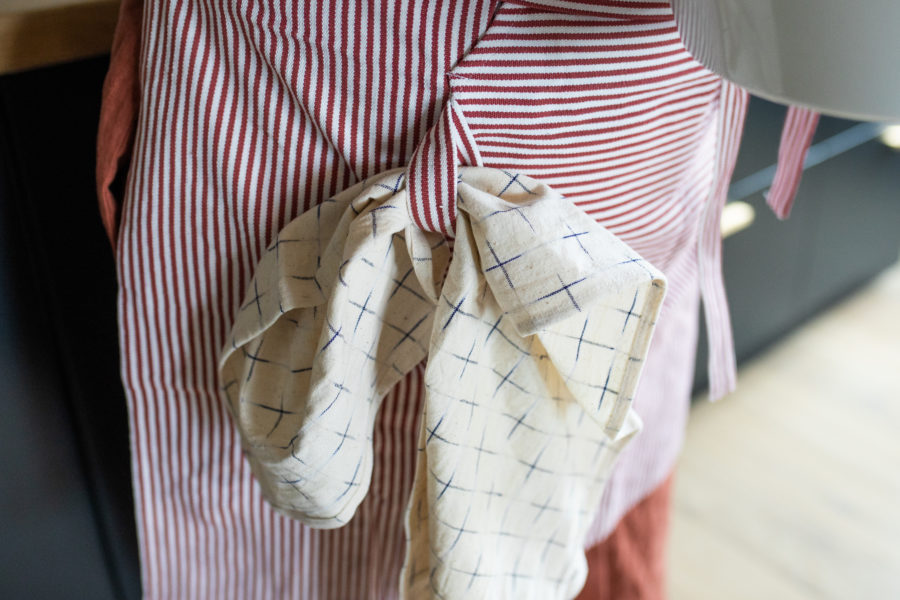 Nærbilde av forkle med røde striper og kjøkkenhåndkle på hanken